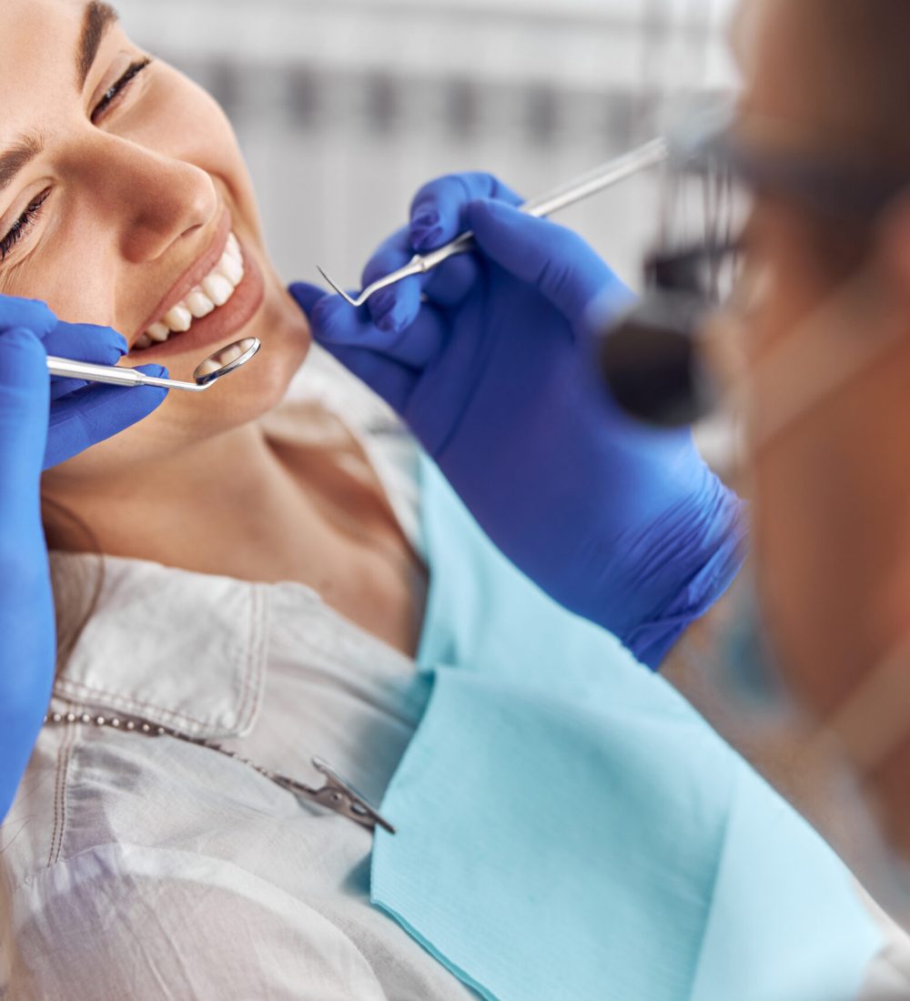 Cheerful positive dentist and client in dentistry. Female patient at dental procedure, doctor using dental instruments in modern dental clinic, close up