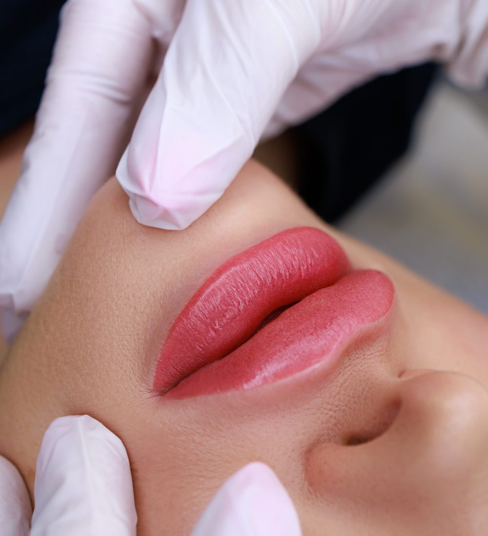 close-up of a permanent make-up of lips made in powder technique, a master in white gloves holds the lips of a model with his fingers