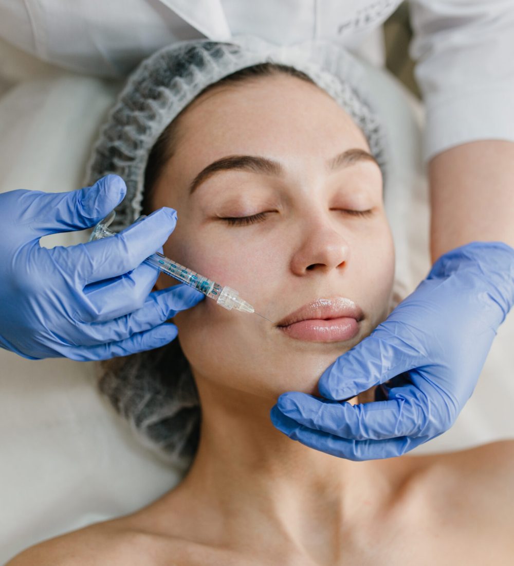 Portrait young woman during cosmetology procedures in beauty salon. Injecting, botox,  hands in blue glows, healthcare, therapy, lips, beauty