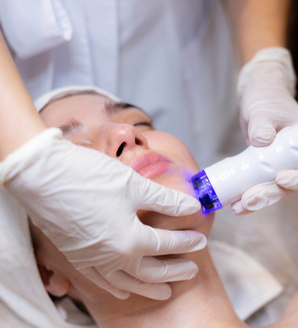 A young beautiful girl lies on the beautician's table and receives procedures with a professional apparatus for skin rejuvenation and moisturizing