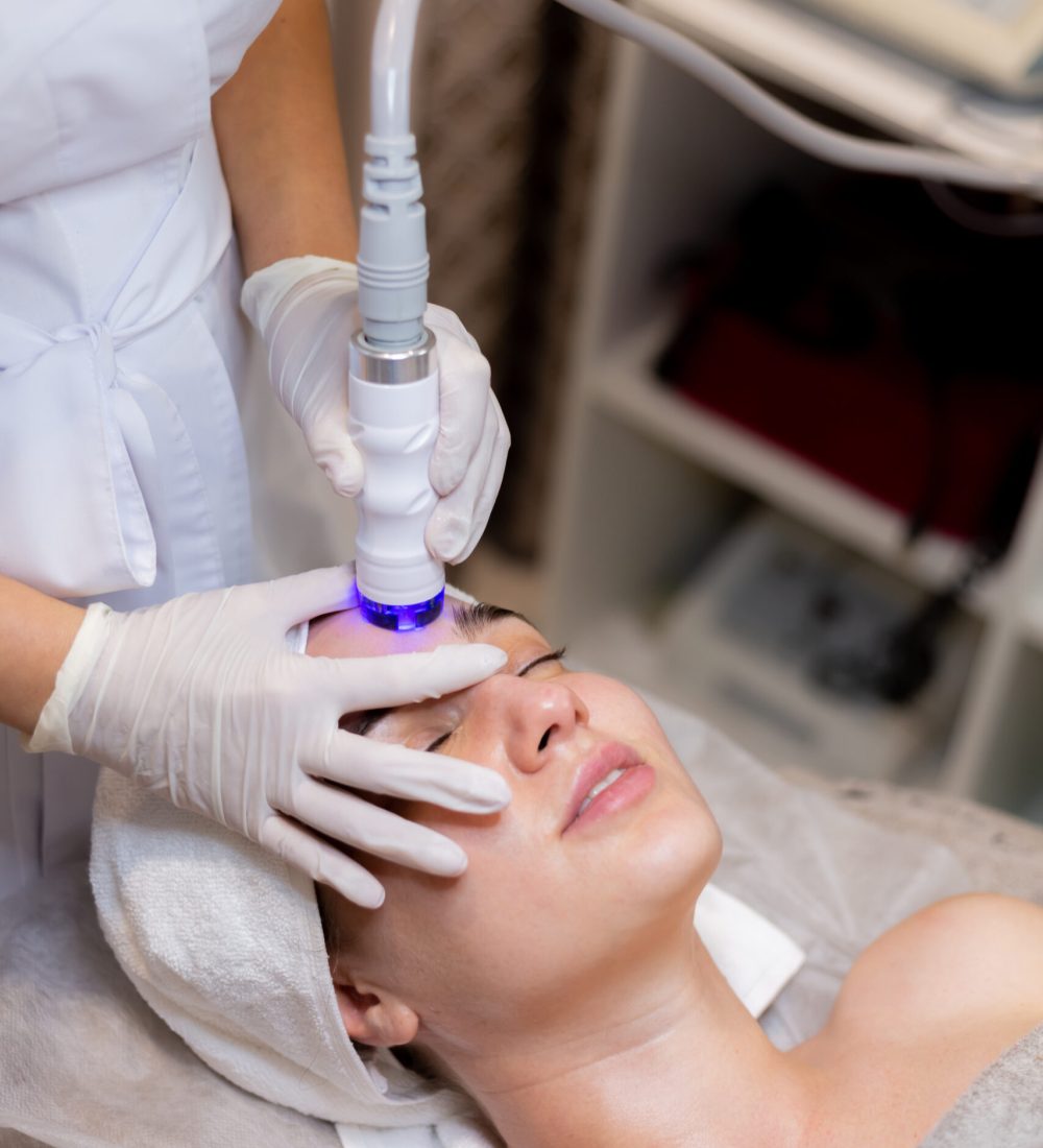 A young beautiful girl lies on the beautician's table and receives procedures with a professional apparatus for skin rejuvenation and moisturizing